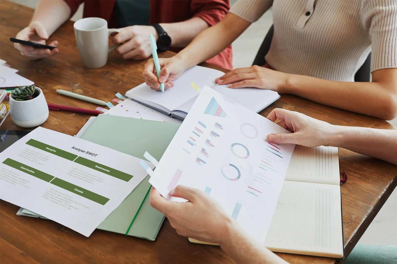 Groupe de personnes travaillant sur un projet avec des documents, graphiques, et un ordinateur portable sur une table en bois.