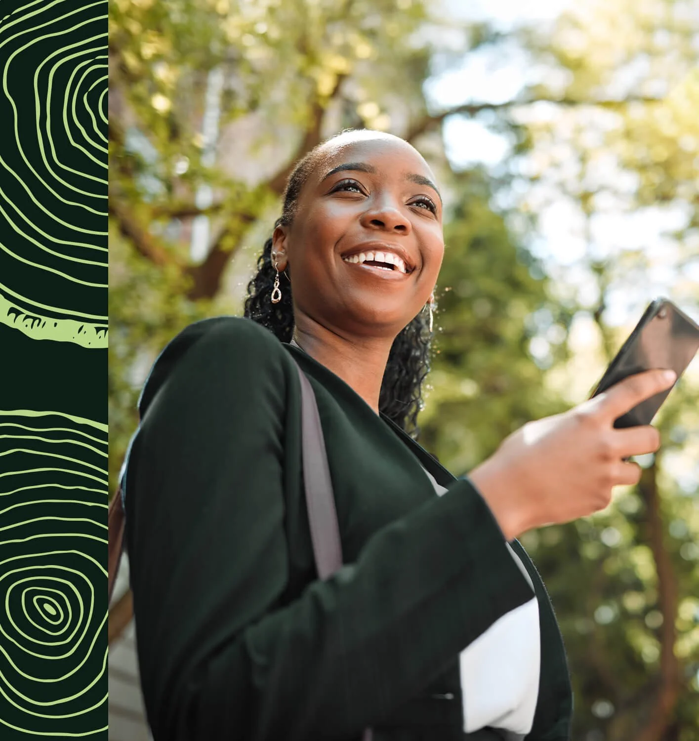Une femme souriante tenant un téléphone portable en extérieur avec des arbres en arrière-plan.