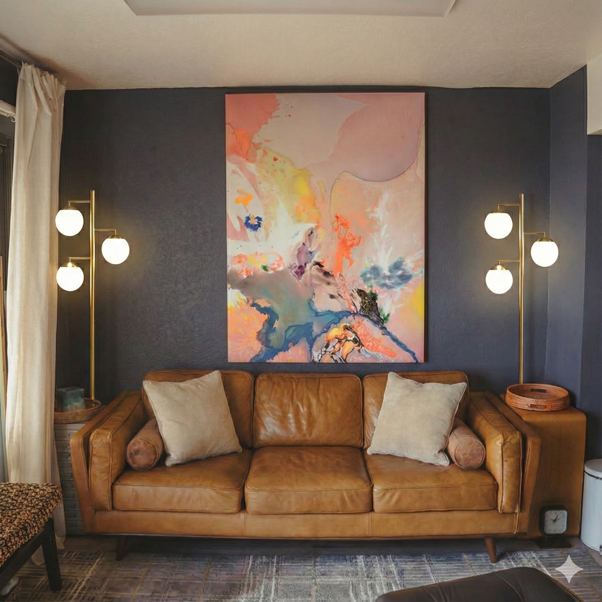 A living room with a brown leather sofa, two beige pillows, and two beige bolster pillows. There are two modern floor lamps with three white globe bulbs on each side of the sofa. Above the sofa, there is an abstract painting with pink, peach, blue, and green tones. To the left, there are cream curtains covering a window, and a small round side table with a woven basket is on the right side of the sofa. The wall behind the sofa is dark, textured wallpaper.