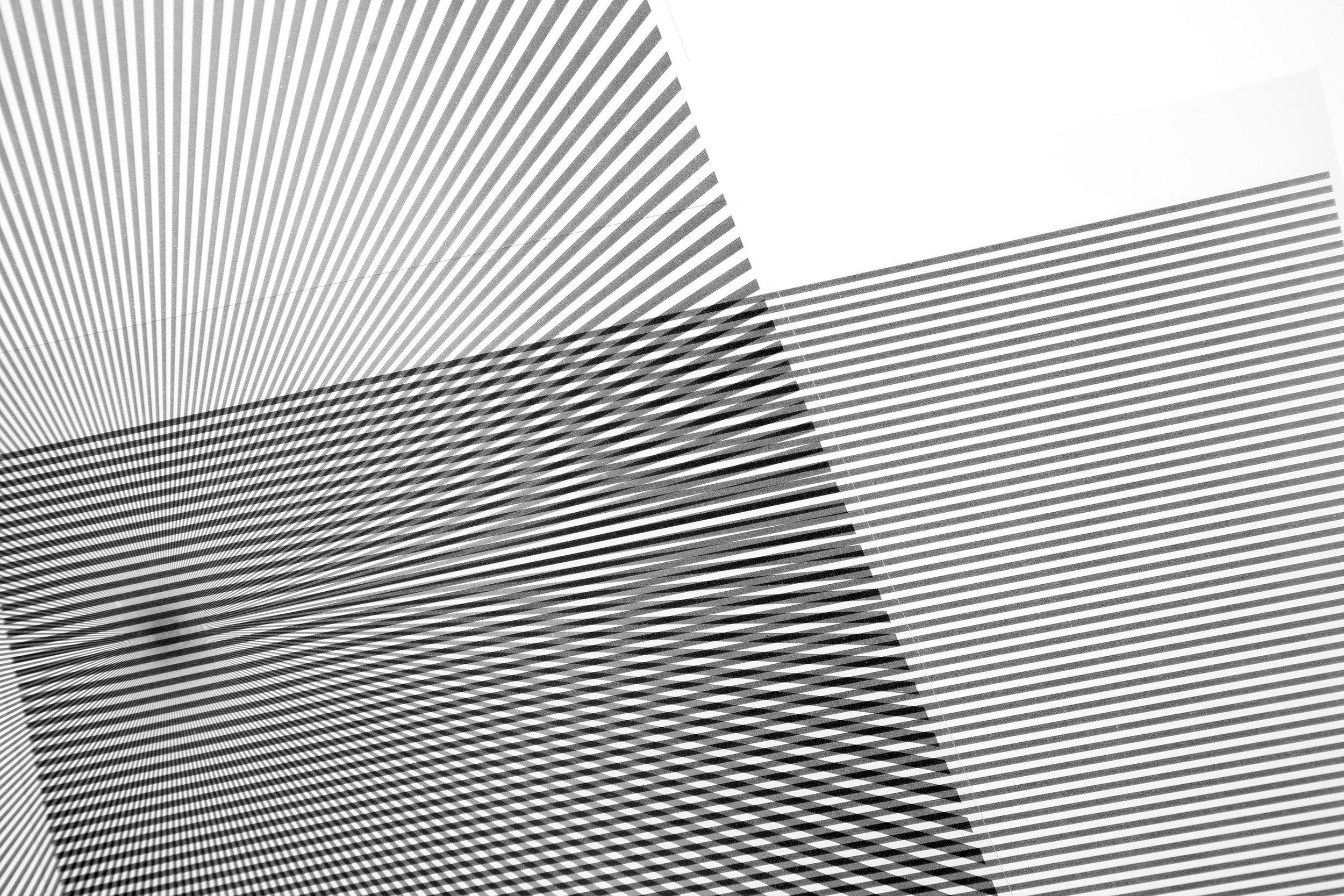 A black and white photograph, cropped to a circle, of two overlapping linear patterns that  produce a moiré effect.