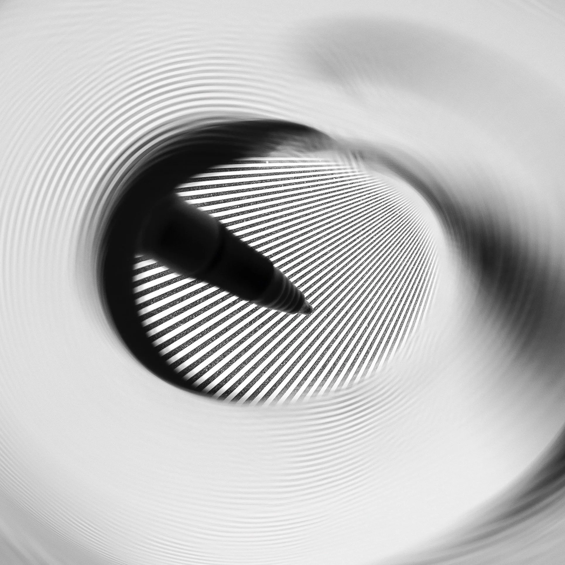 A circular black and white image of a pen in shadow inside a swirl of black and white stripes and in front of a background of black lines going back in perspective.