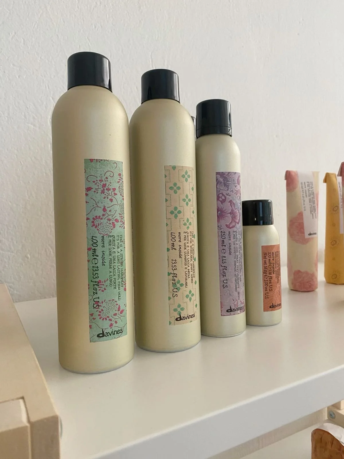 Four beige color bottles with black caps and decorative labels on a white shelf.