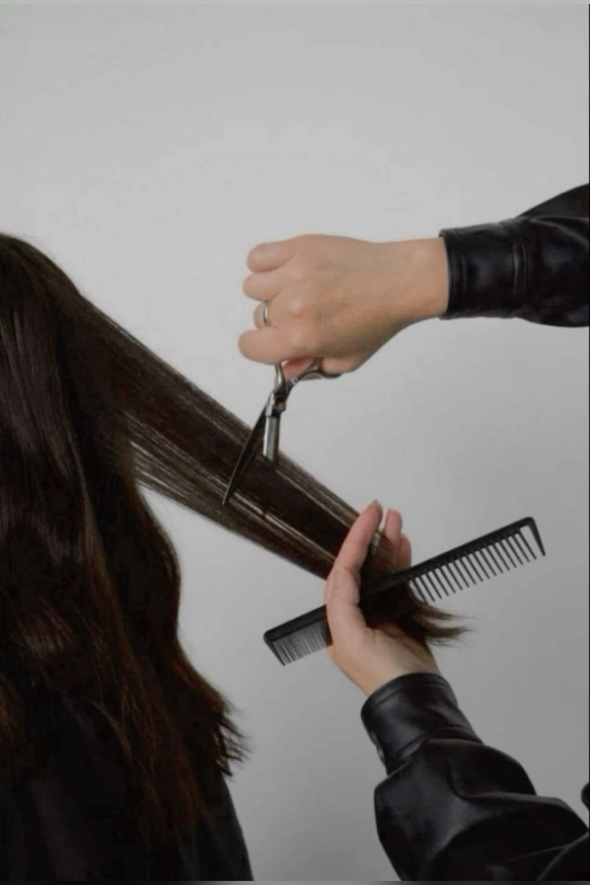 A person getting their hair cut with scissors, a comb, and a section of dark brown hair.