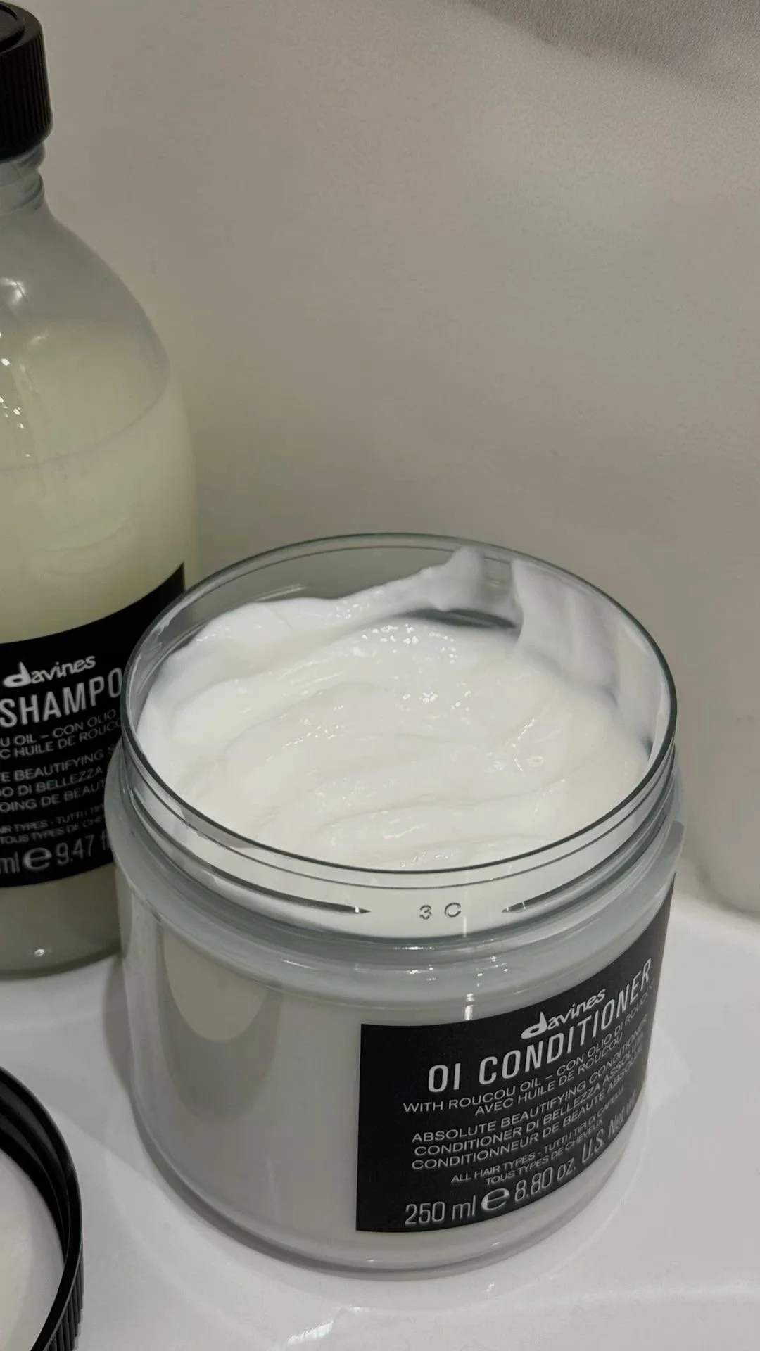 Open jar of Davines OI Conditioner with creamy white hair conditioner, next to a bottle of Davines Shampoo.