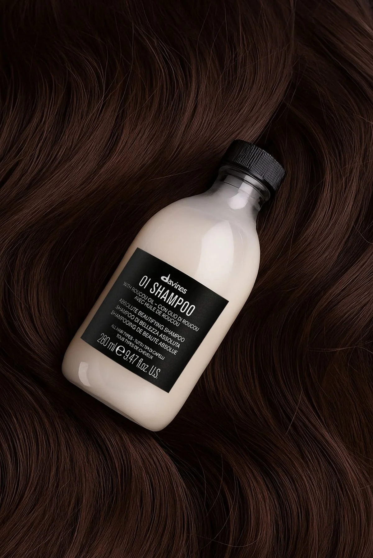 Brown hair with a bottle of Davines shampoo placed on it.