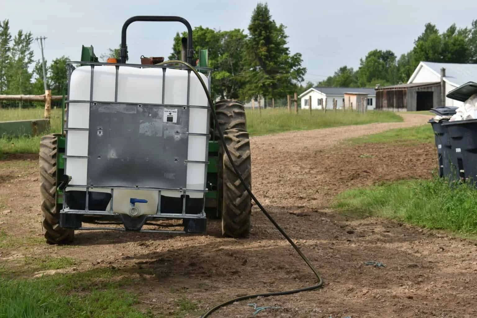 Tractor with a white IBC tote spray tank mounted on the back and a hose coiled in the dirt
