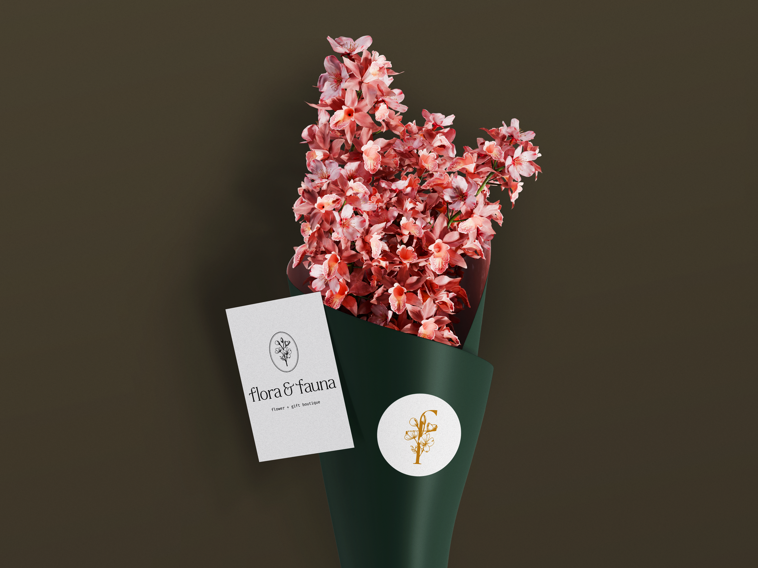 A pink orchid bouquet in a dark green wrapping with a white and gold logo, accompanied by a white card that reads 'flora & fauna, flower + gift boutique'.