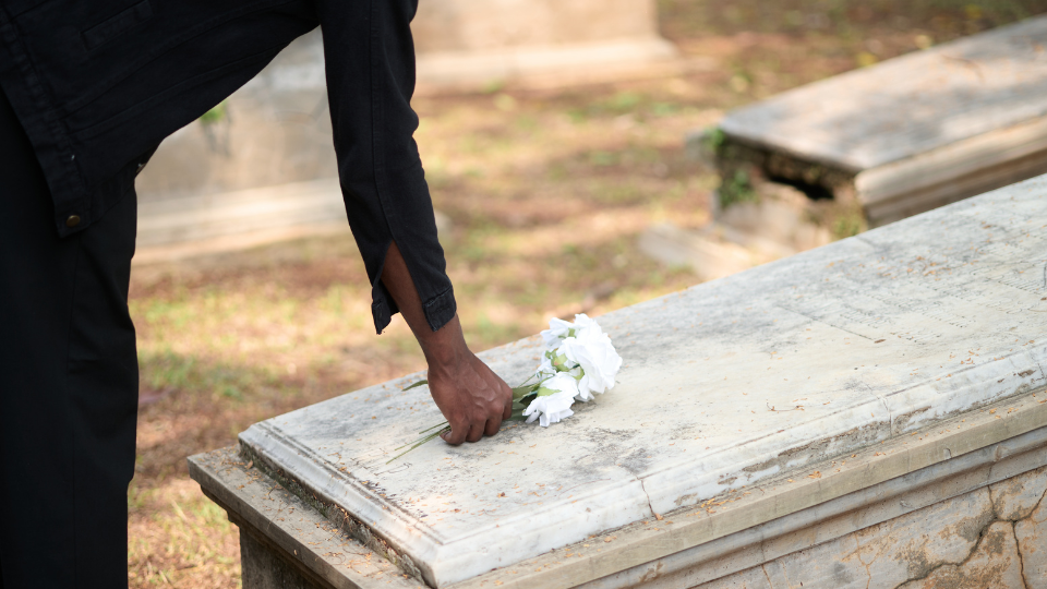 Person placing white flowers on a gravesite at a cemetery.