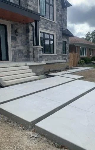 concrete sidewalk in front of a modern house with stone exterior.
