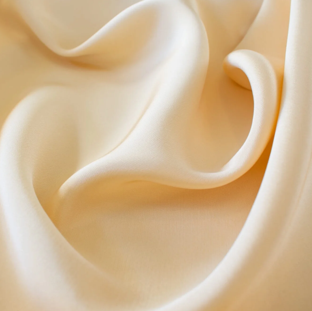 Close-up of a cream-colored silk fabric with smooth, flowing curves and folds.