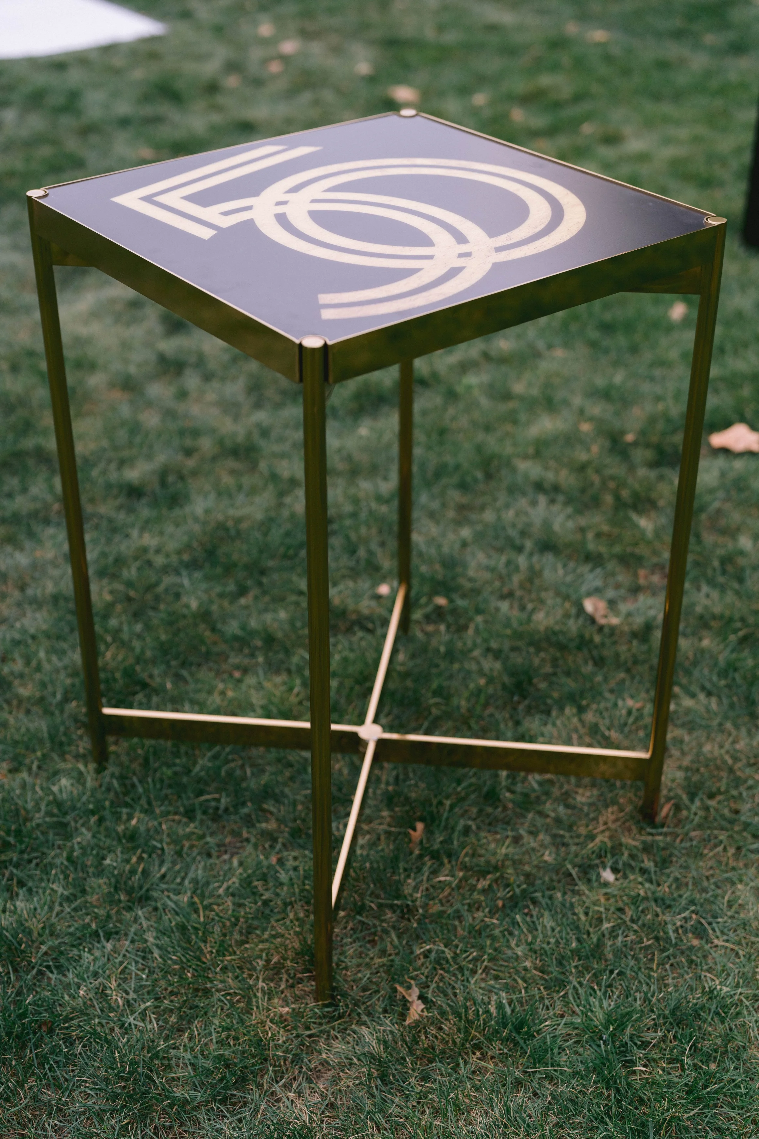 A modern table with a black top featuring white geometric line art, set outdoors on grass.