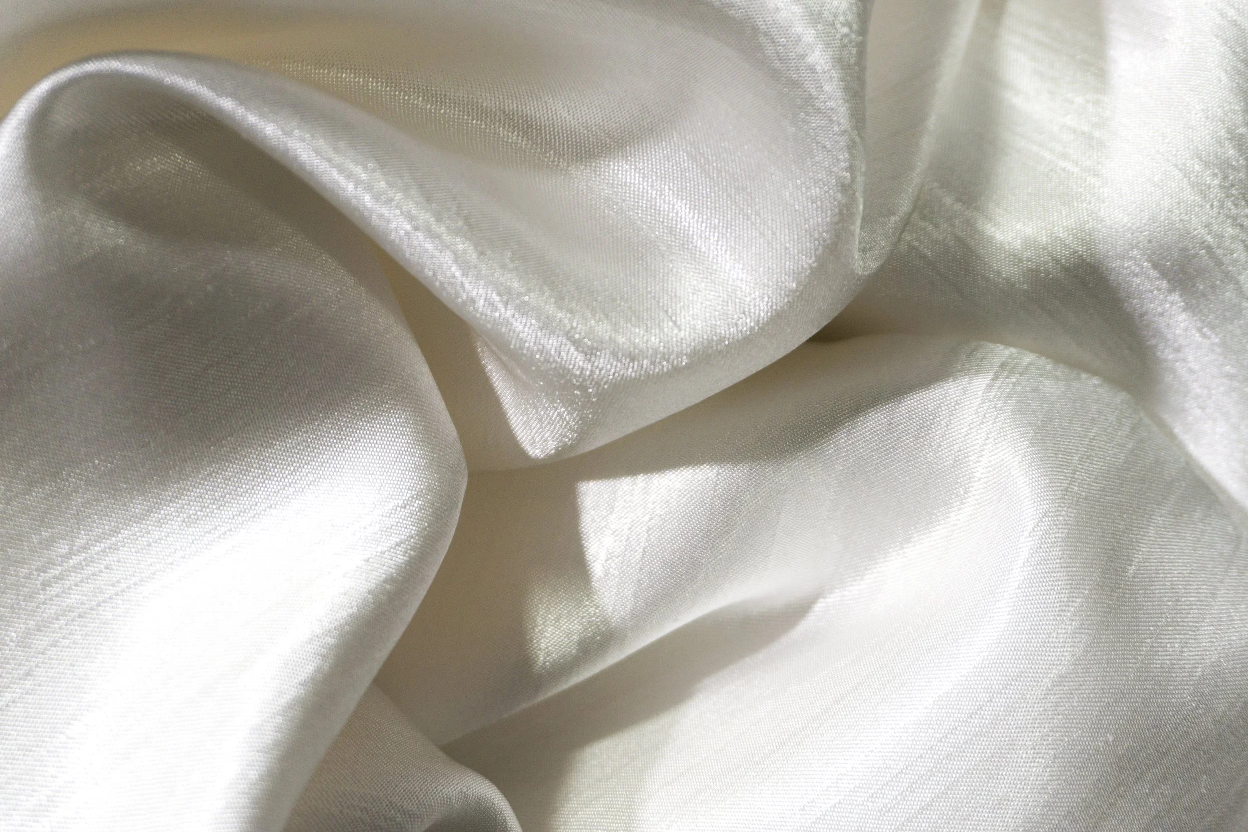 Close-up of shiny white satin fabric with smooth, flowing folds.