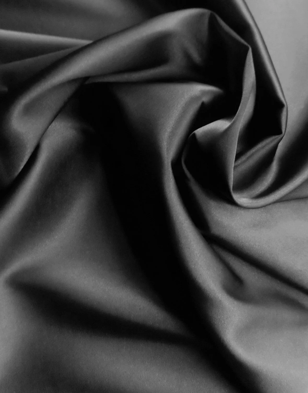 Close-up of black satin fabric with smooth, shiny texture, twisted into folds and creases.