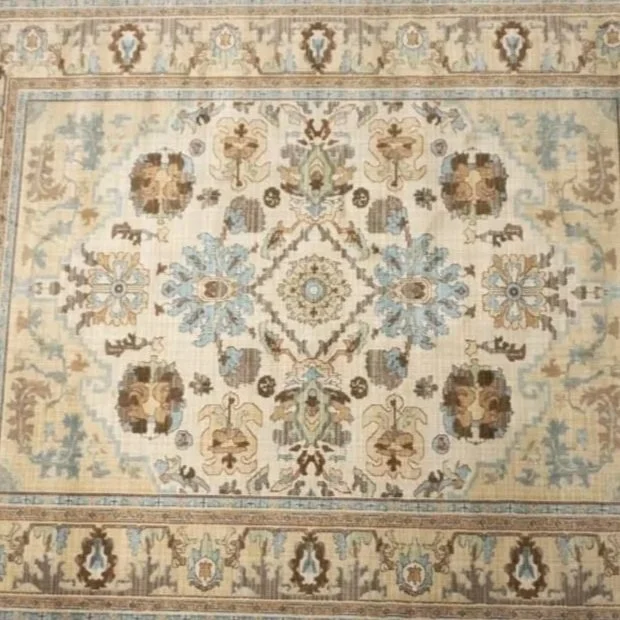 A traditional patterned area rug with floral and geometric motifs in beige, blue, brown, and cream colors.
