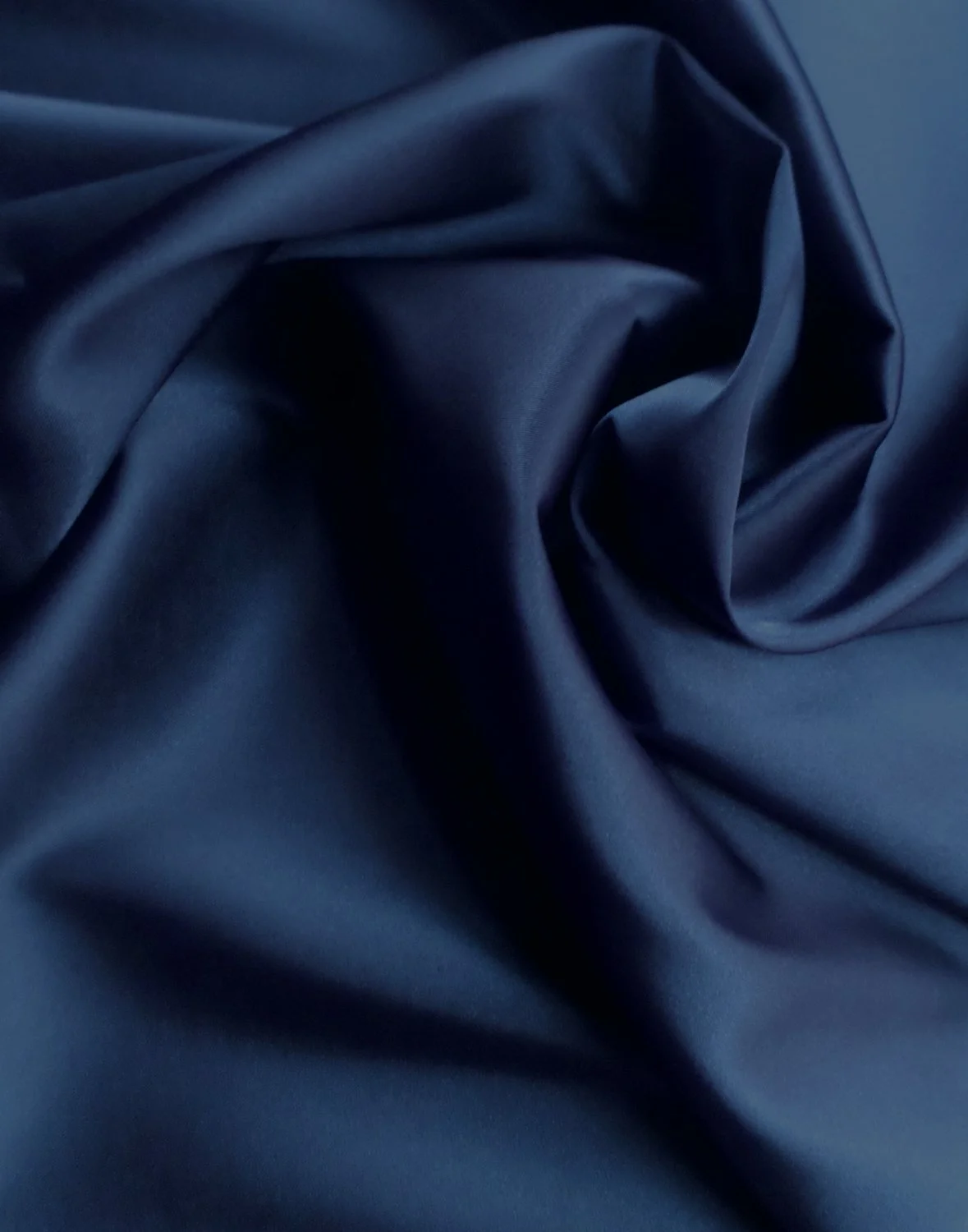 Close-up of dark blue silky fabric with smooth, shiny surface and gentle folds.