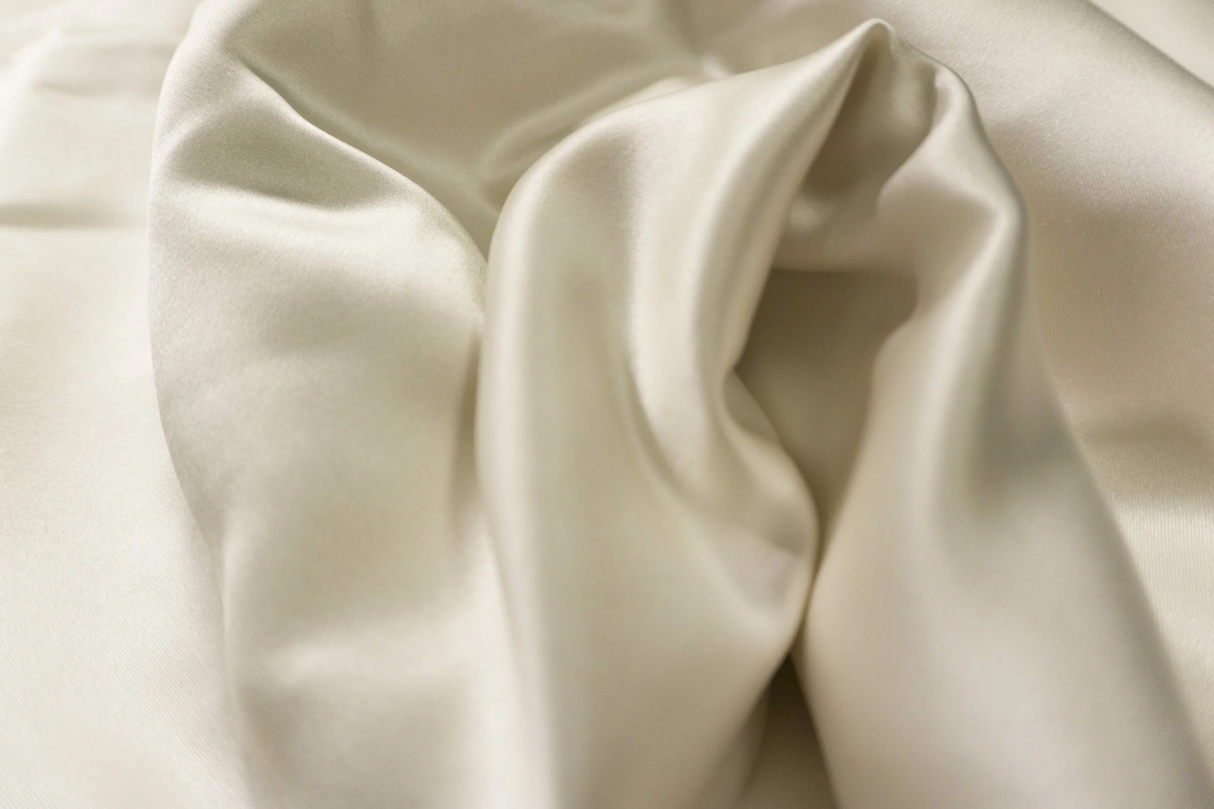 Close-up view of smooth, ivory-colored silk fabric with soft folds and sheen.