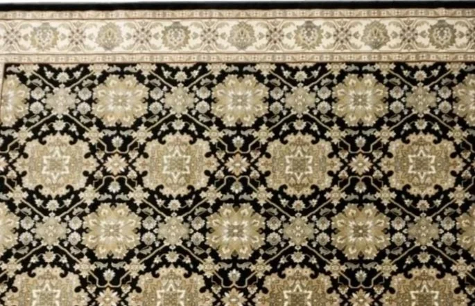 Close-up of a decorative patterned rug with black, cream, and beige colors and geometric floral designs.