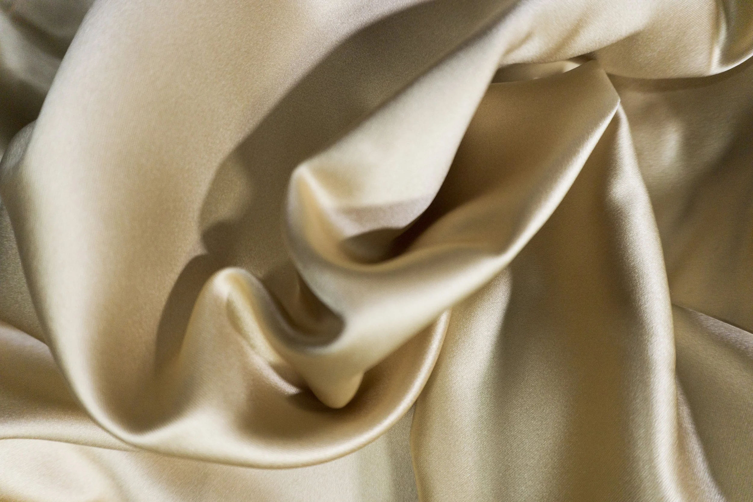 Close-up of beige silk fabric with soft folds and smooth texture.