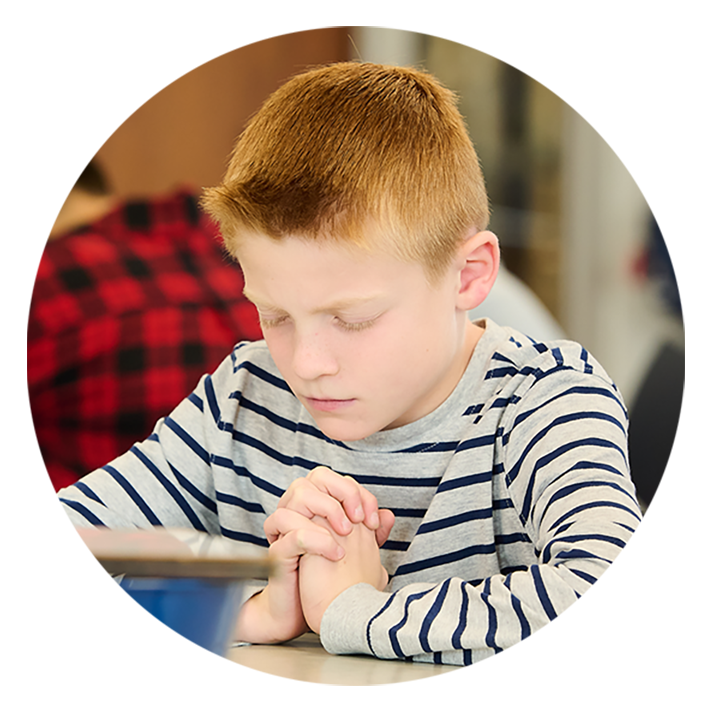 A young LCCS student with his hands clasped and head bowed in prayer