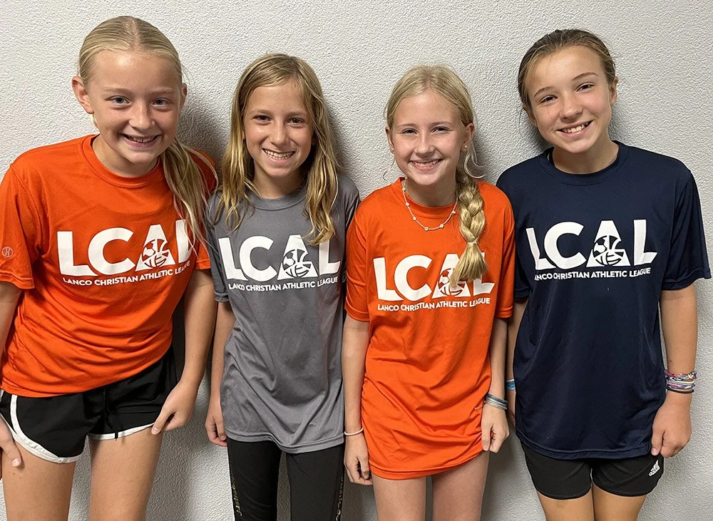 Four LCCS girls standing side by side wearing Lanco Christian Athletic League T-shirts, smiling