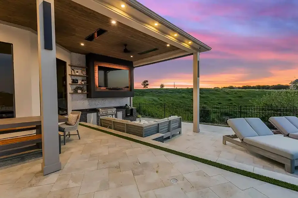 Sunset showing behind a moder patio cover with outdoor kitchen and TV with backlighting