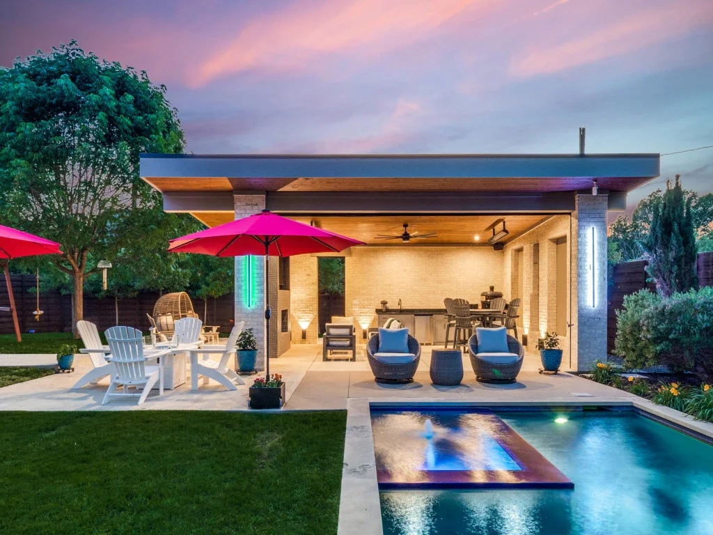 A freestanding patio cover and pool at night, with ambient lighting.