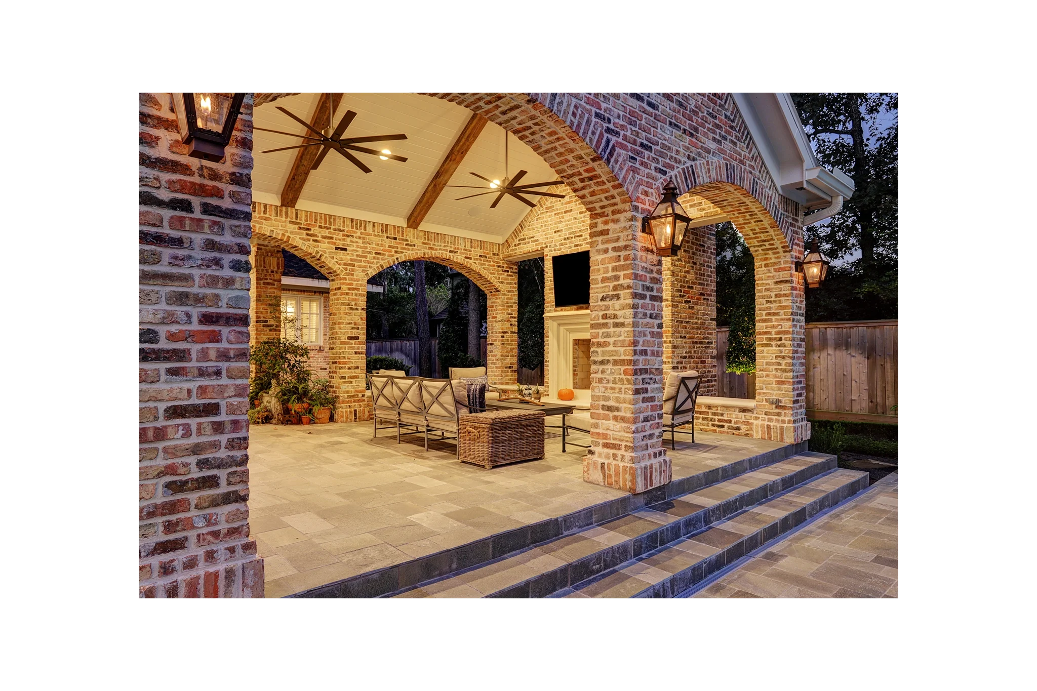 Luxury custom patio cover built to match the home’s brick, featuring elegant arches, paver flooring, and a cast stone outdoor fireplace, positioned next to a pool and spa with decorative water features.