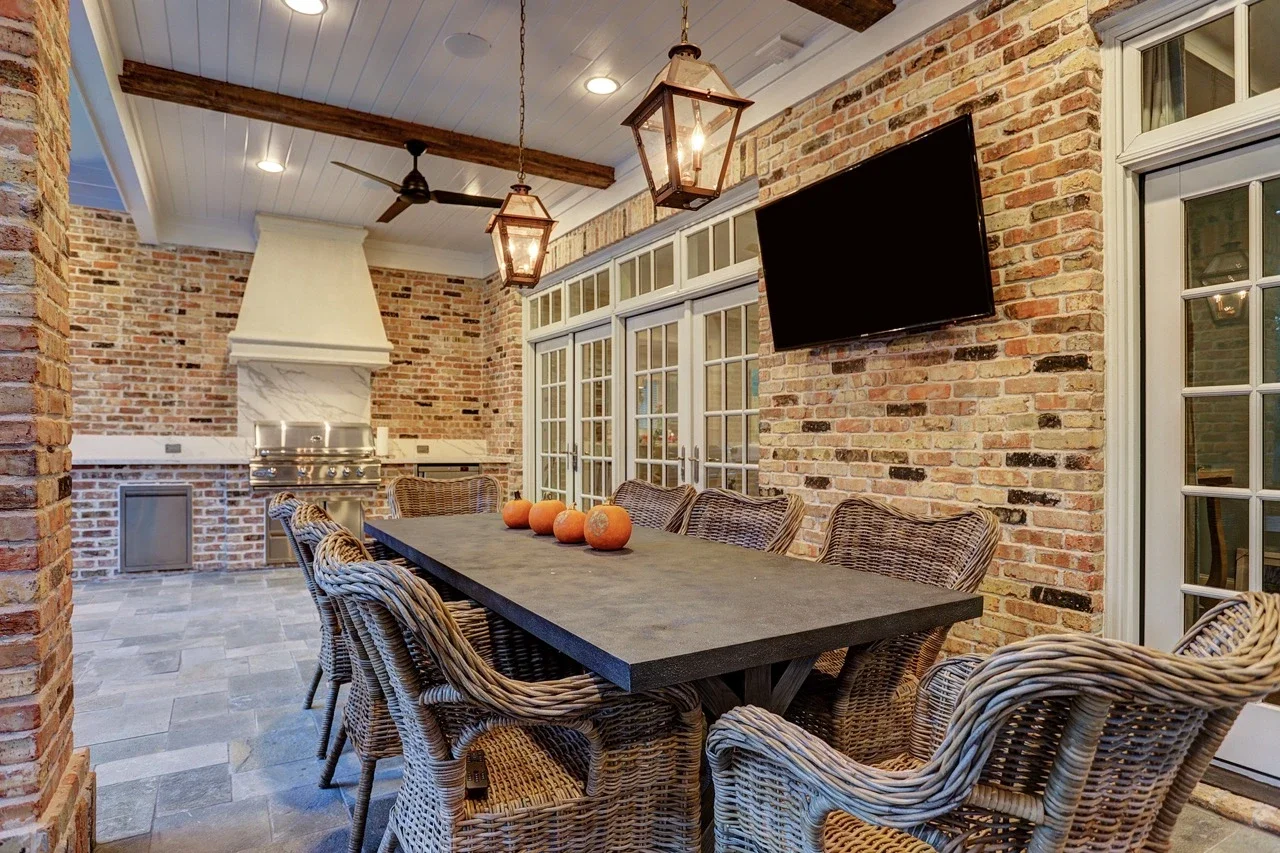 Seamless outdoor living space with a custom brick patio cover, arched architectural details, pavers, and a cast stone fireplace, designed to look original to the home and placed alongside a pool and spa with fountains.