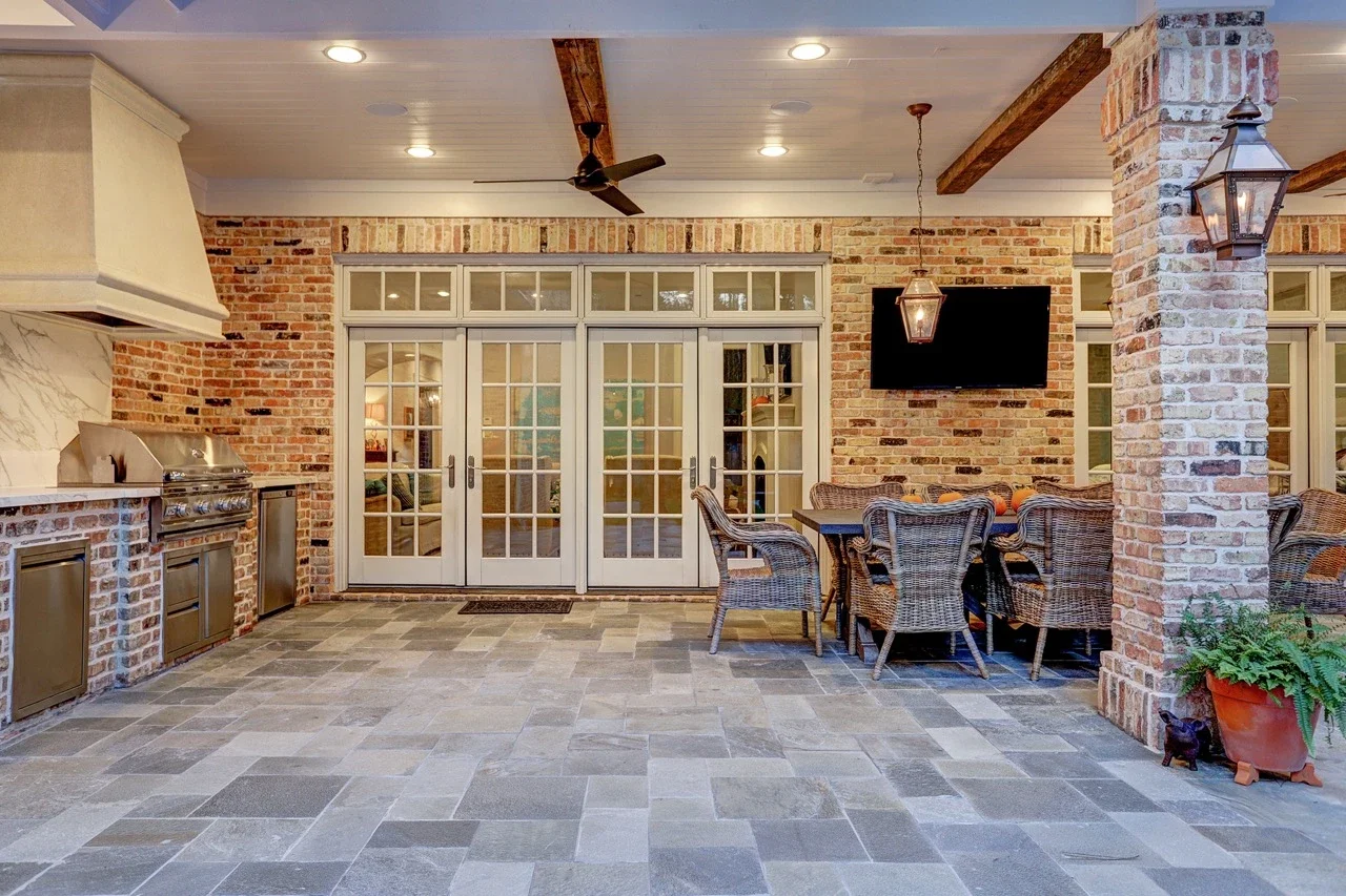 Seamless outdoor living space with a custom brick patio cover, arched architectural details, pavers, and a cast stone fireplace, designed to look original to the home and placed alongside a pool and spa with fountains.
