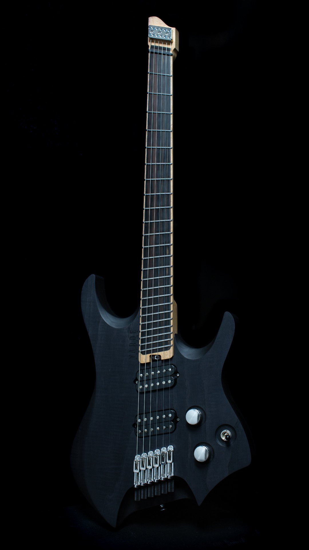 A headless - multiscale electric guitar with a black stain finish, two humbucker pickups, a fixed bridge, maple neck and ebony fretboard, against a black background - Portrait view