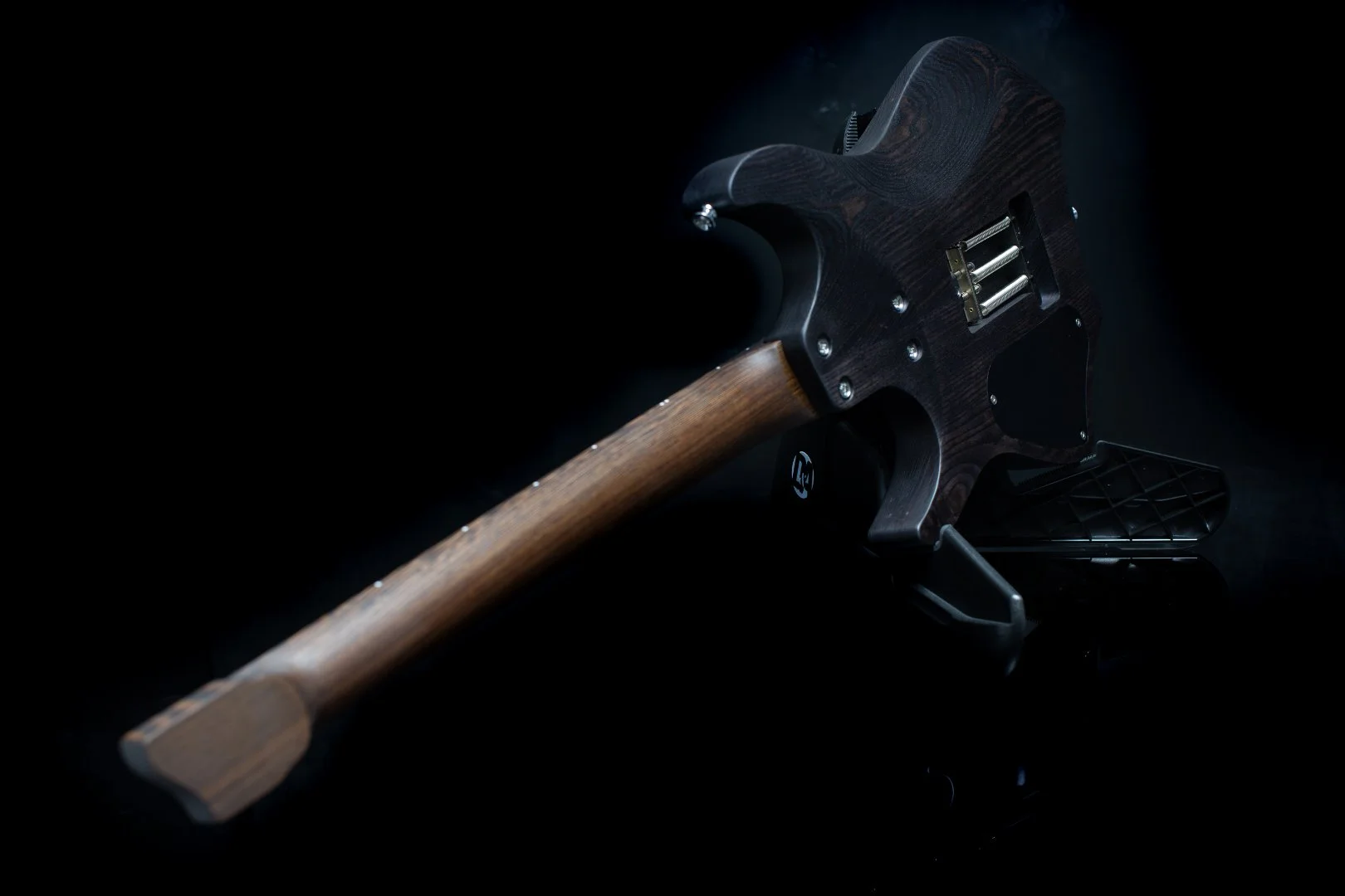 close up neck view of a headless electric guitar with a black stain finish