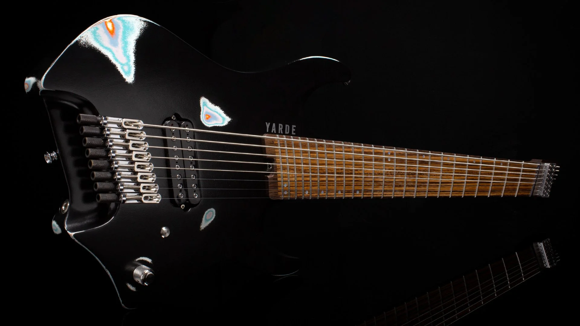 A 8 string headless - multiscale electric guitar with a black painted finish and multicolour relic patterns - landscape view