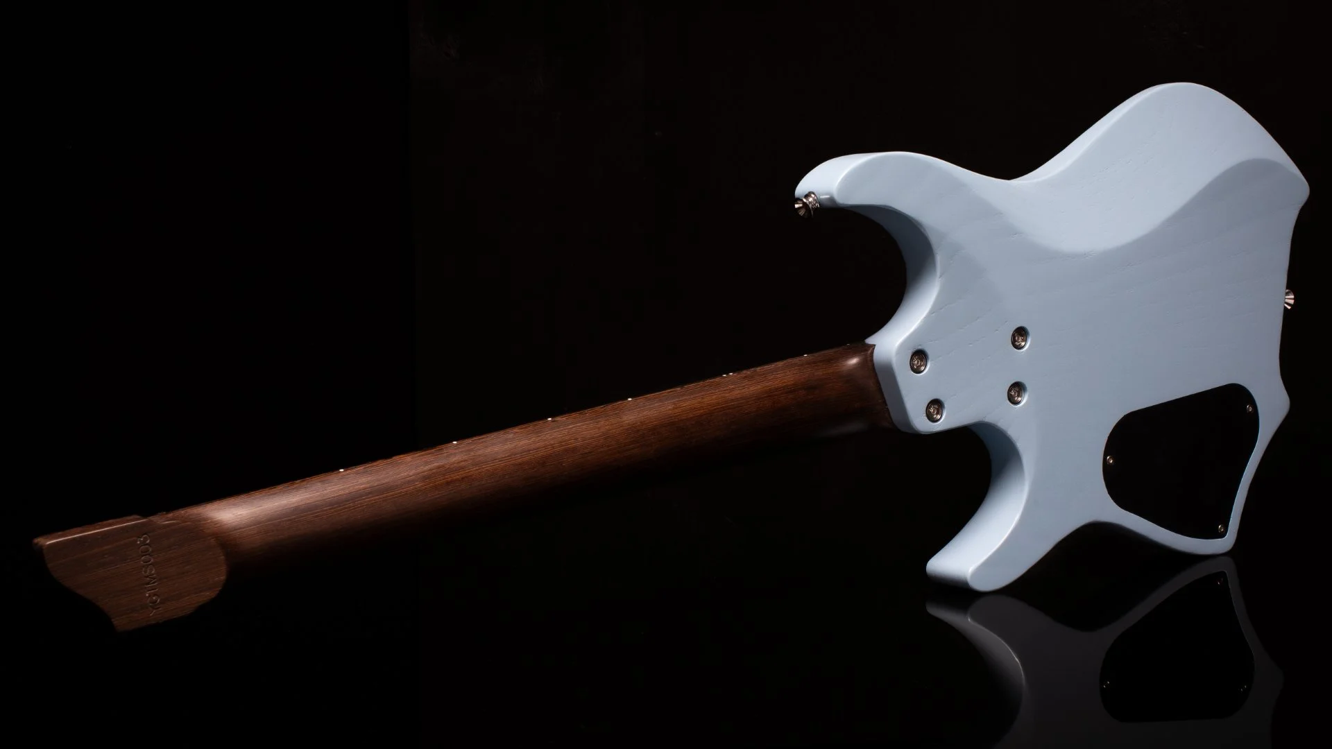 Close-up of the back of a headless - multiscale electric guitar with a light blue painted swamp ash body, wenge neck and chrome hardware against a black background - Landscape back view