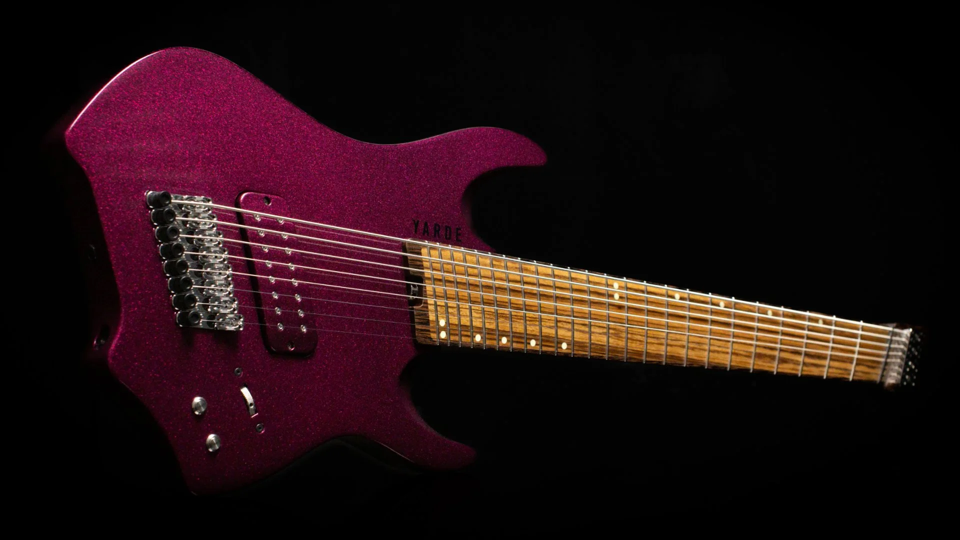 A bright pink headless 8 string guitar with a matching painted pickup cover in a landscape view