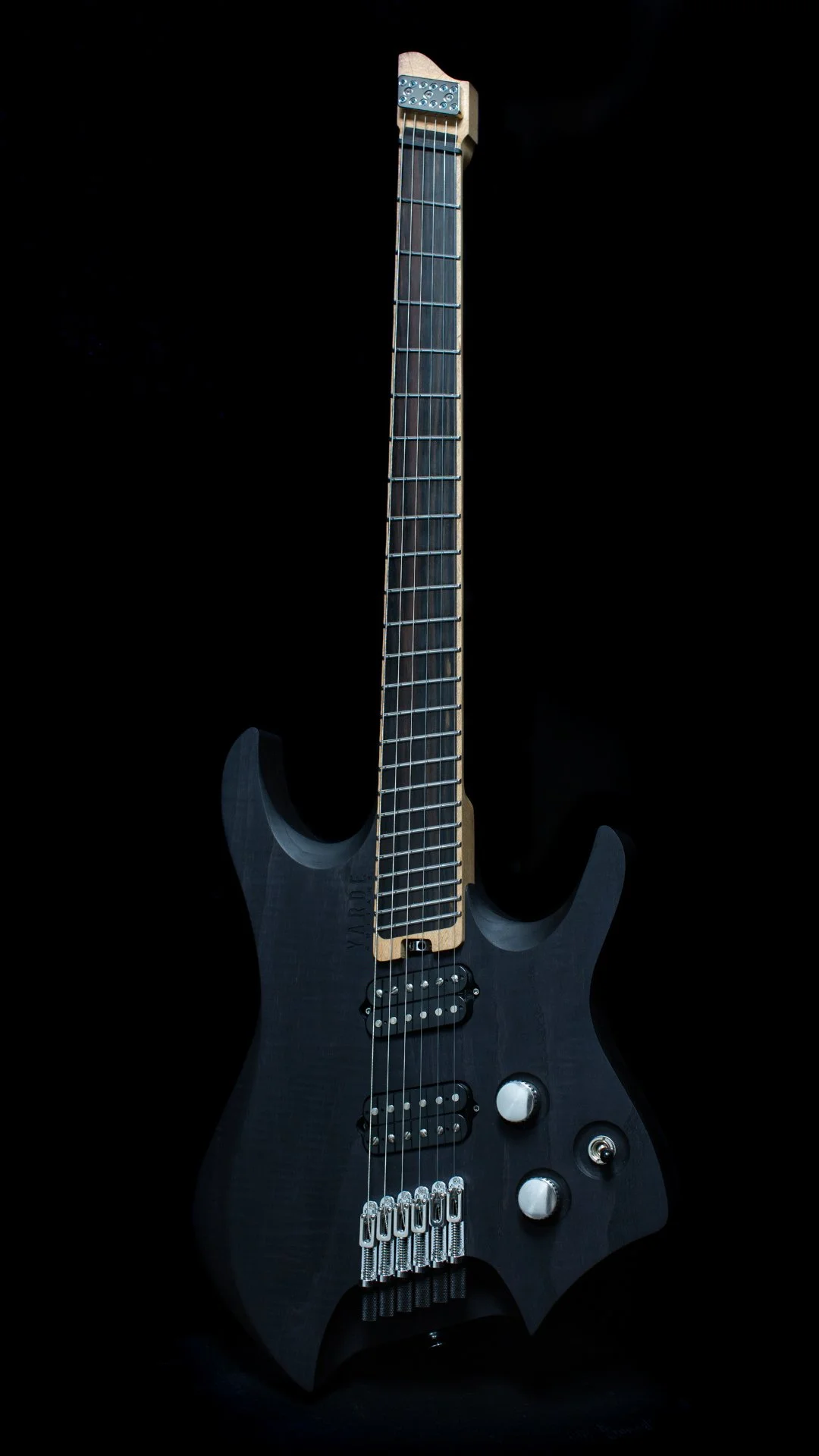 A headless - multiscale electric guitar with a black stain finish, two humbucker pickups, a fixed bridge, maple neck and ebony fretboard, against a black background - Portrait view