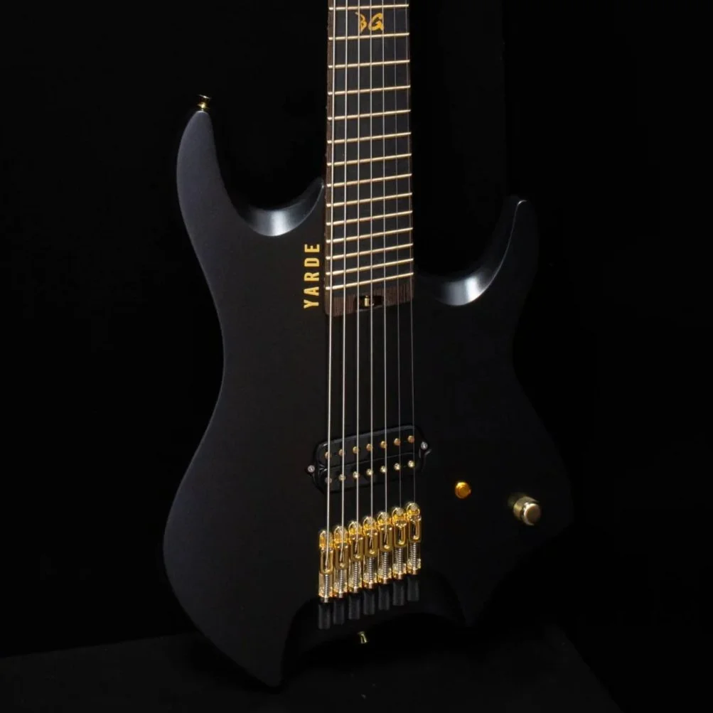 A close-up of a black headless electric guitar with gold hardware against a black background - Body view