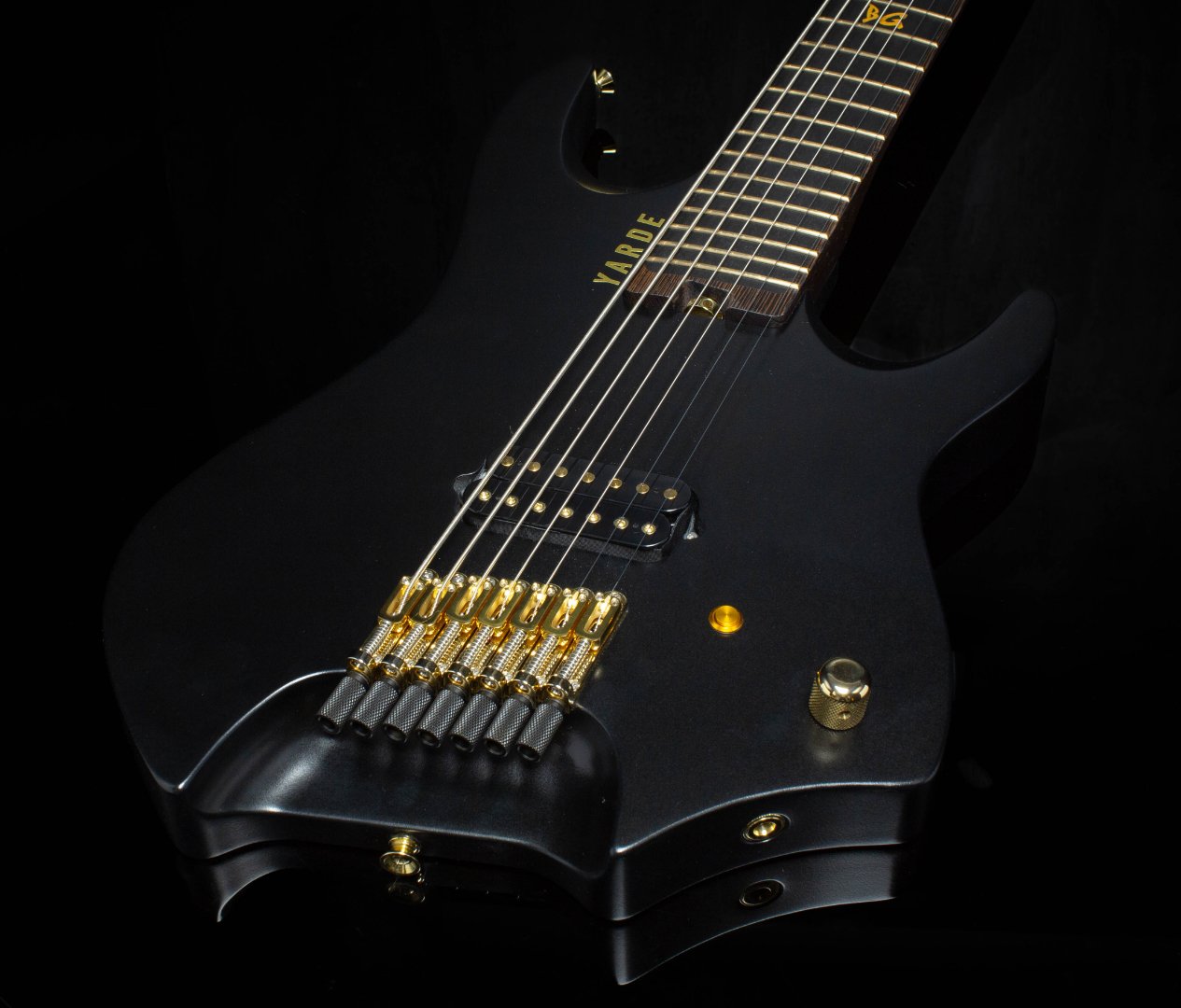 A black 7 string headless - multiscale electric guitar showing the gold hardware- 3/4 Front View
