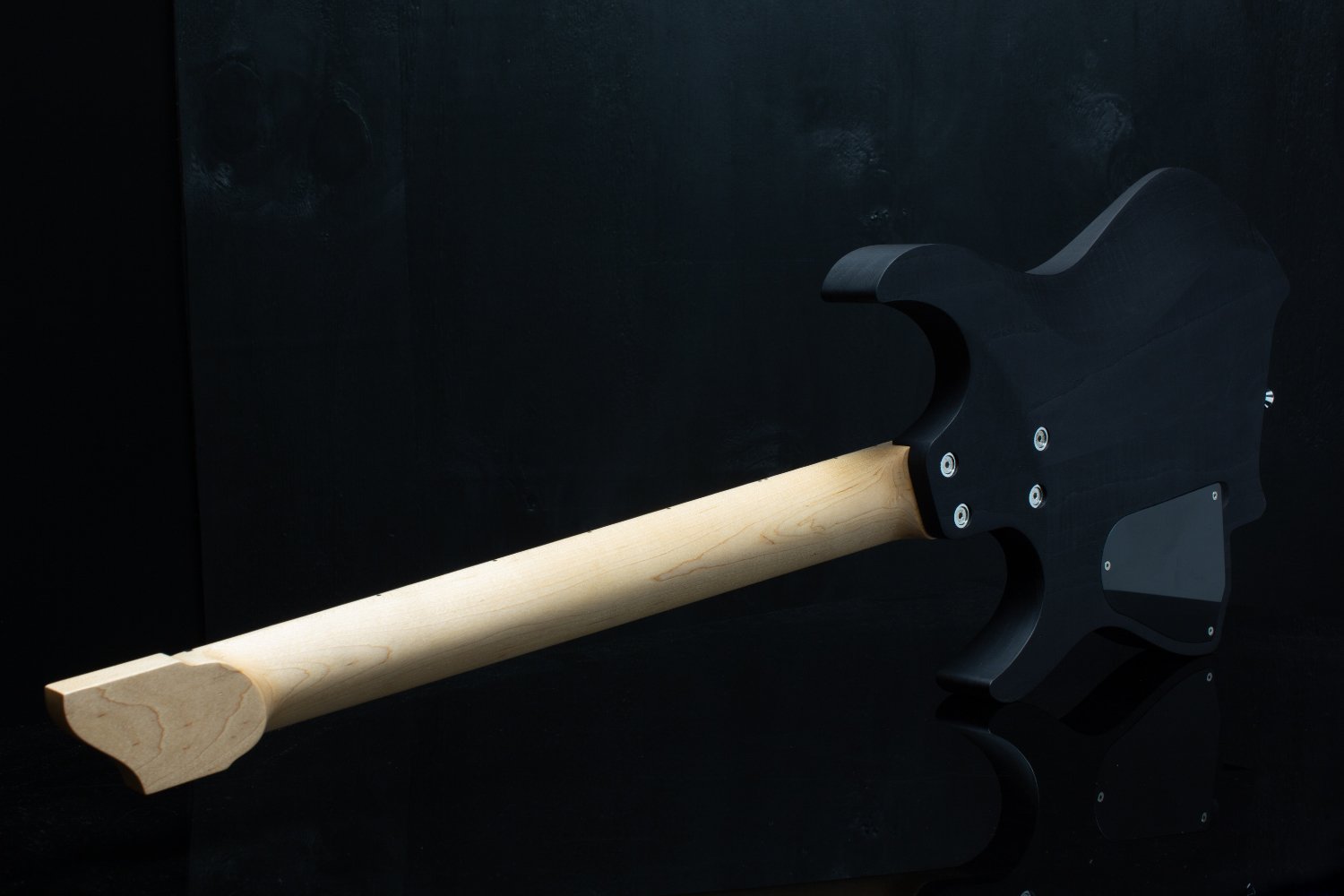 Close-up of the back of a headless - multiscale electric guitar with a black stained swamp ash body, maple neck and chrome hardware against a black background - Landscape back view