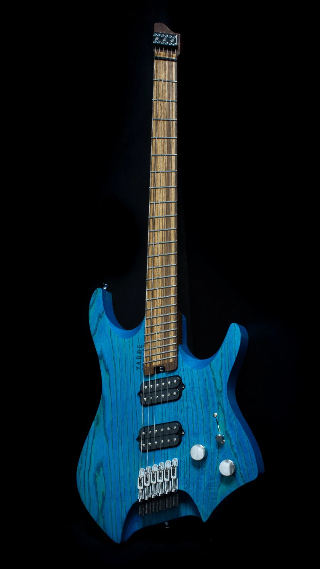 A headless - multiscale electric guitar with a blue stain finish, two humbucker pickups, a fixed bridge, wenge neck and zebrano fretboard, against a black background - Portrait view