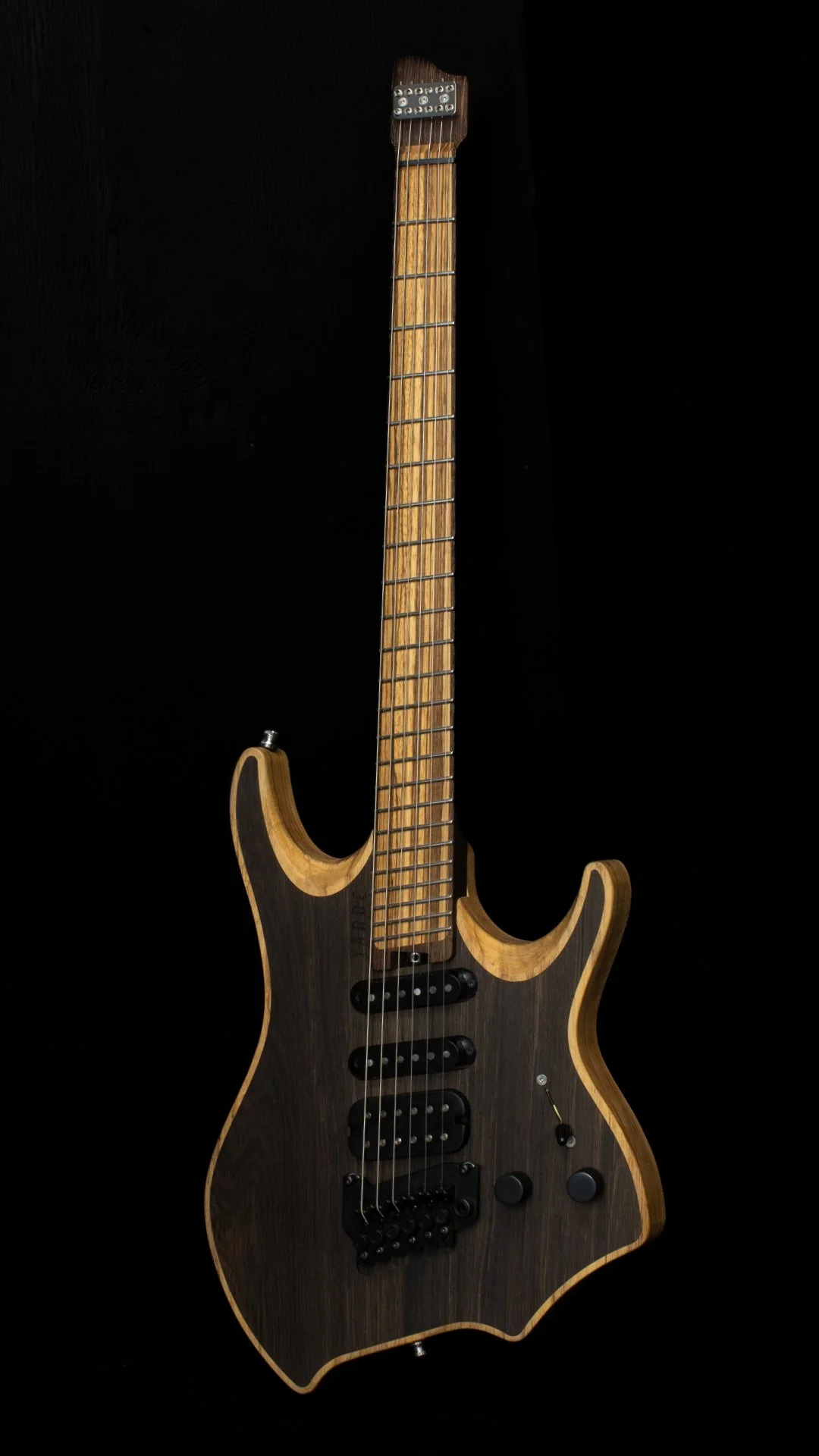 A headless guitar with an inlaid bog oak cap, oil finished, two humbucker pickups, a chrome tremolo bridge, Wenge neck and inlaid zebrano fretboard, against a black background - Portrait view