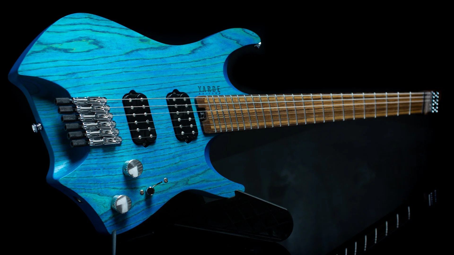 A headless - multiscale electric guitar blue stained ash body in an oil finish, two humbcuker pickups and a black background - Landscape view