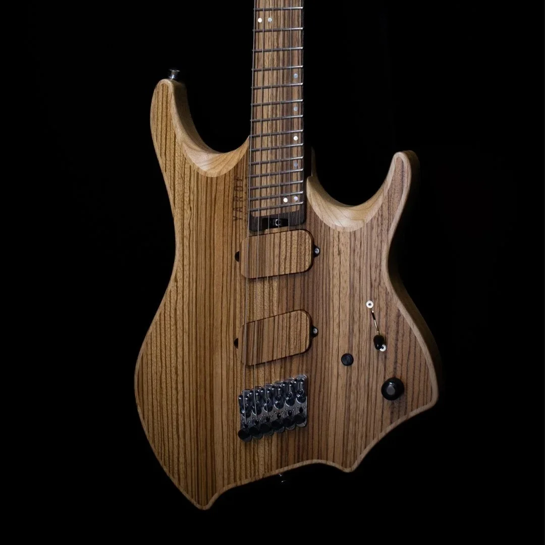 A close-up of a headless electric guitar with an inlaid cap in a  natural wood finish against a black background - Body view