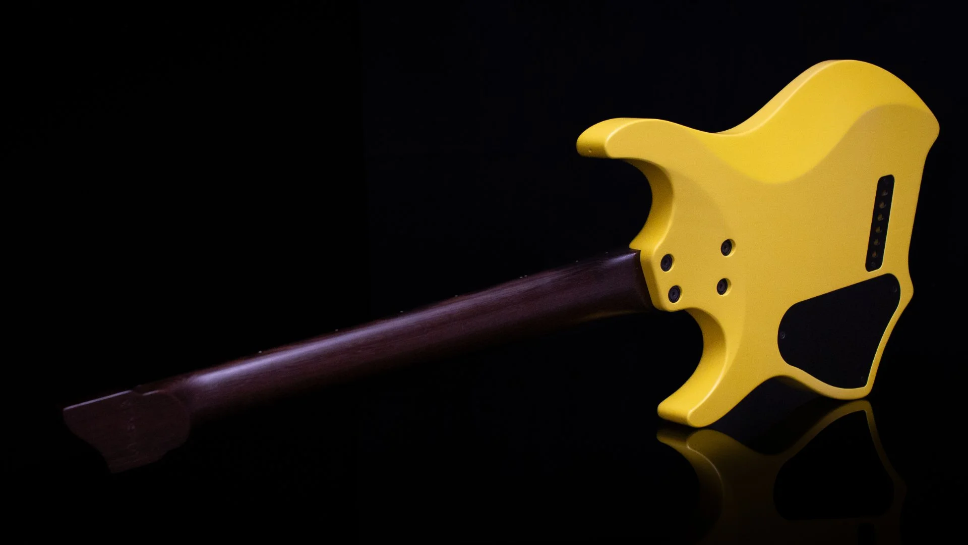 Close-up of the back of a headless - multiscale electric guitar with a bright yellow painted swamp ash body, wenge neck and black hardware against a black background - Landscape back view
