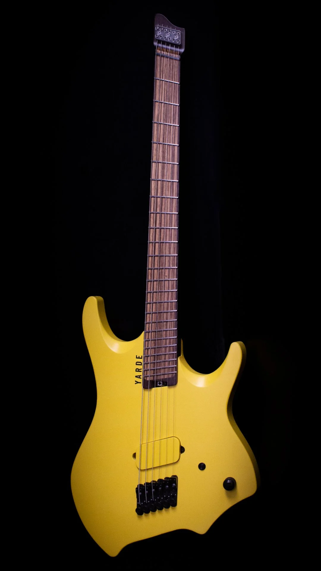 A bright yellow headless - multiscale electric guitar with a wooden covered custom humbucker pickup, standing up right against a black background