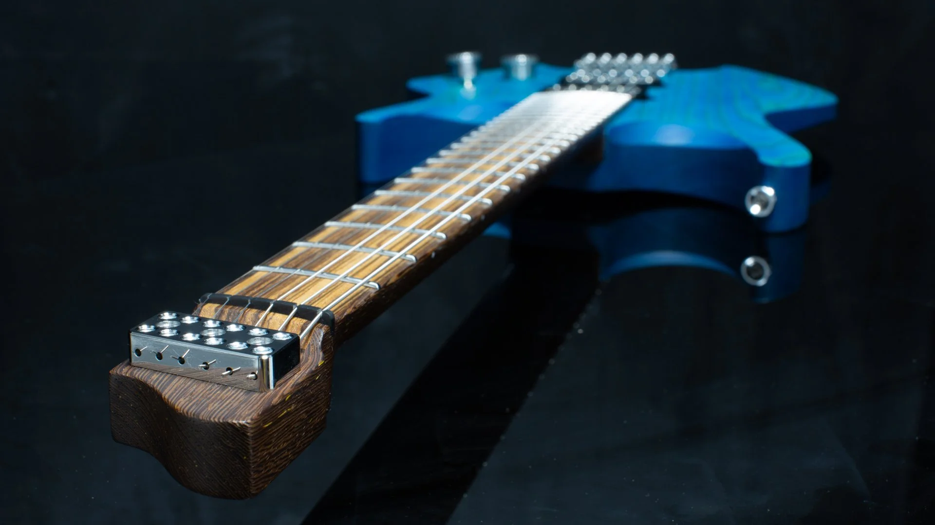 A blue stained headless - multiscale elctric guitar focussing on the zebrano inlaid fretboard - neck view