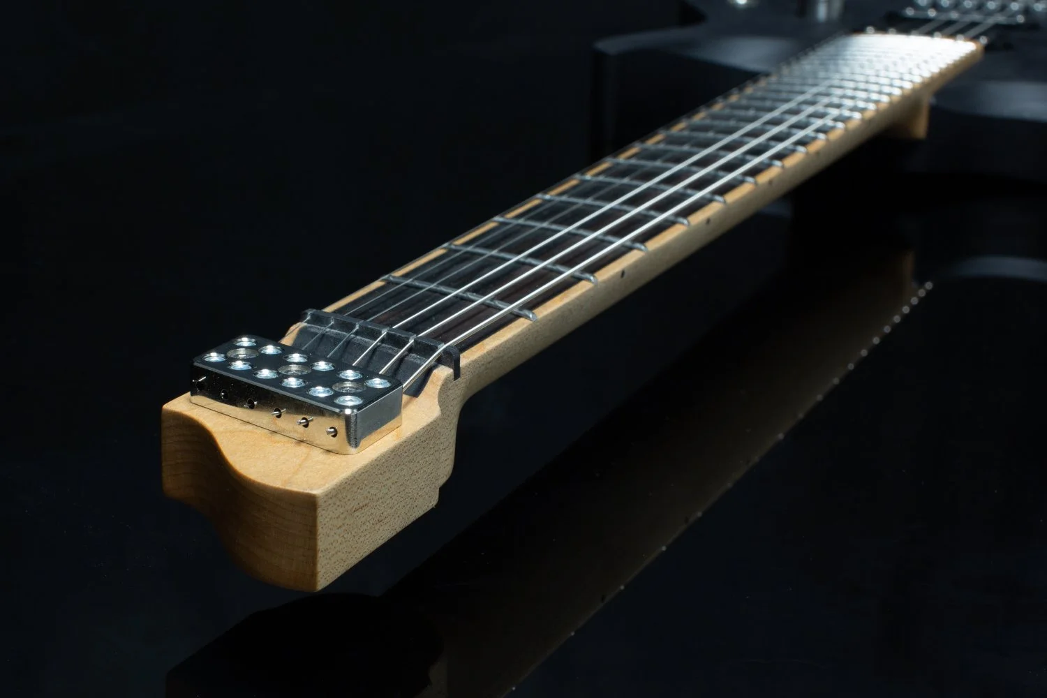 Close-up of a headless - multiscale electric guitar with an inlaid ebony fretboard with a chrome fixed bridge against a dark background - Neck and headstock view