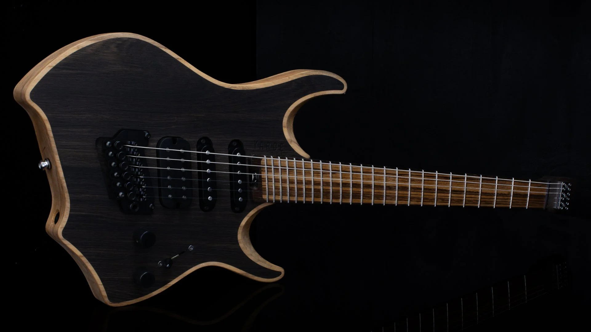 A headless - multiscale electric guitar with an inlaid bog oak cap in a natural finish, HSS pickups and a black background - Landscape view