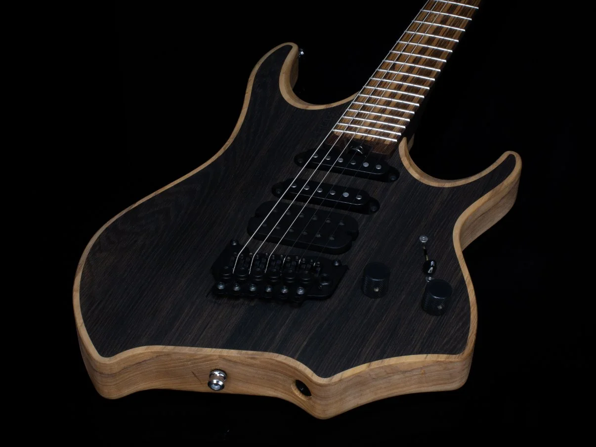 A natural finished headless - multiscale electric guitar against a black background, featuring an inlaid bog oak cap and black hardware - 3/4 view of body