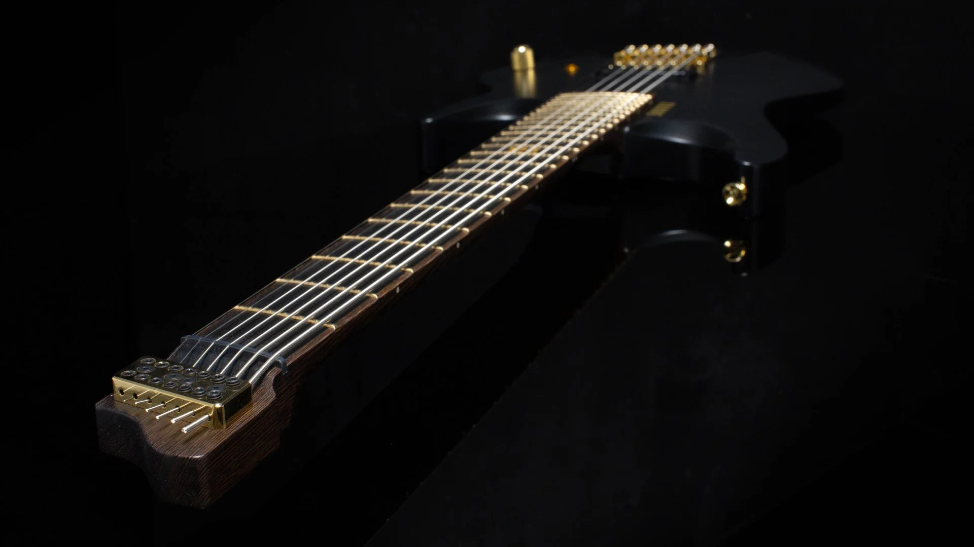 A black painted 7 string headless - multiscale electric guitar focussing on the inlaid black richlite fretboard