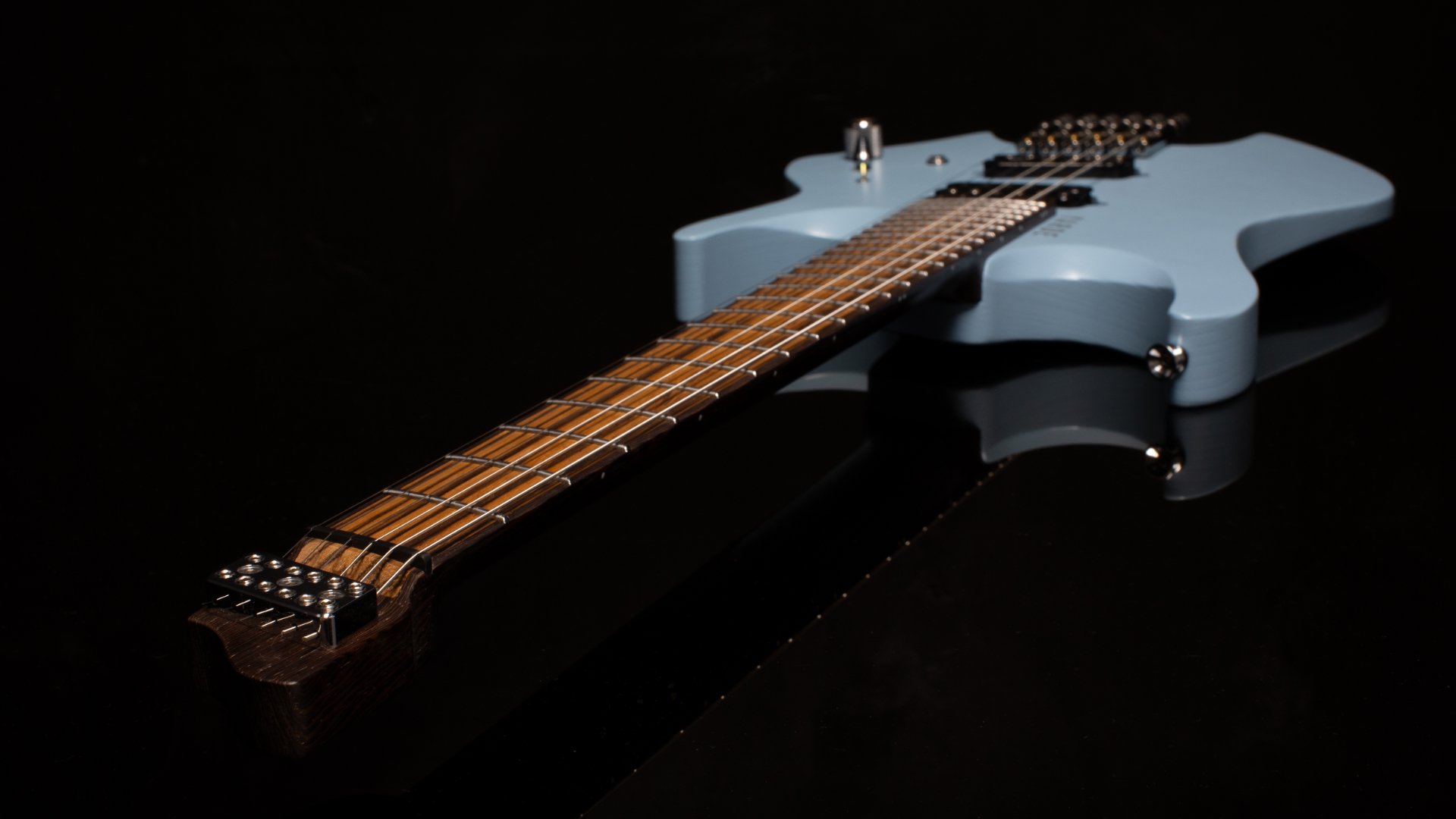 Close-up of a light blue painted headless - multiscale electric guitar with an inlaid zebrano fretboard with a chrome fixed bridge against a dark background - Neck and headstock view
